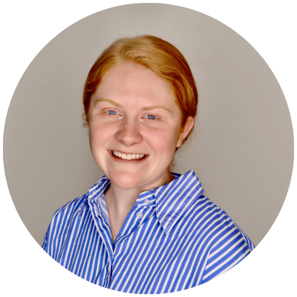 Natalie Sheridan's  headshot. A young woman with ginger hair, blue eyes, and a wide smile, wearing a blue and white striped shirt against a gray background.